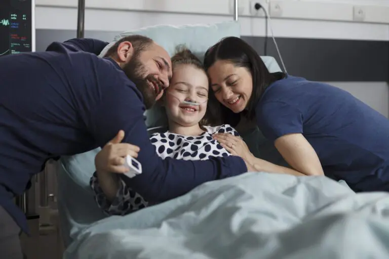 Happy sick little girl hugged by joyful smiling parents in hospital pediatrics ward